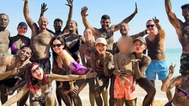 Grupo de influencers en la playa, cubiertas de lodo, posando sonrientes frente al mar.