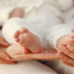 Manos de un adulto sosteniendo los pies de un bebé, símbolo de natalidad